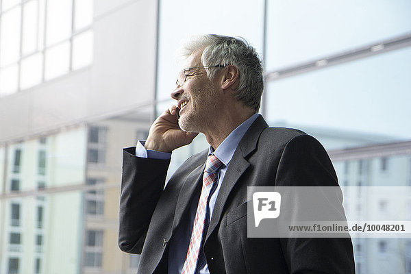 Businessman standing at window using mobile phone