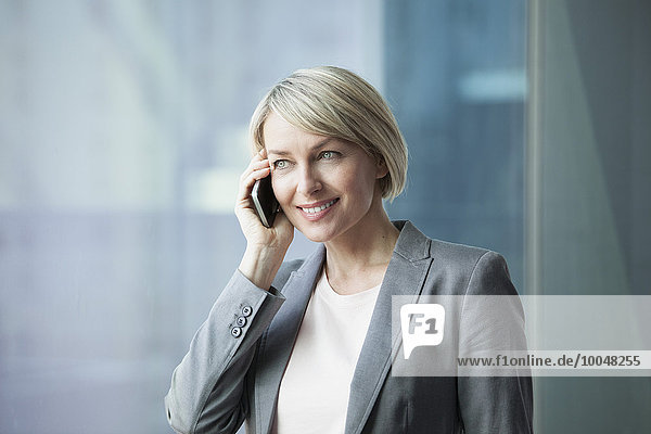 Businesswoman standing at window using mobile phone