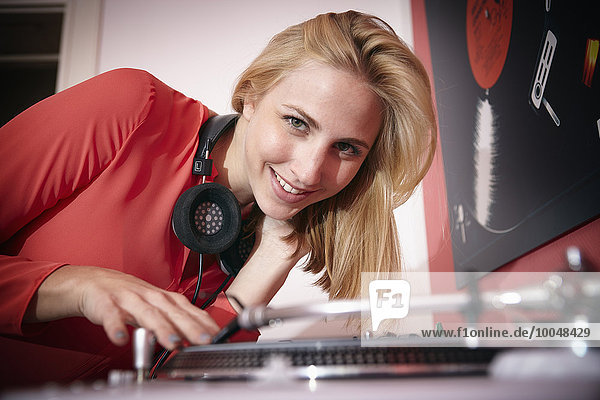 Porträt einer lächelnden jungen Frau mit Kopfhörer und Plattenspieler