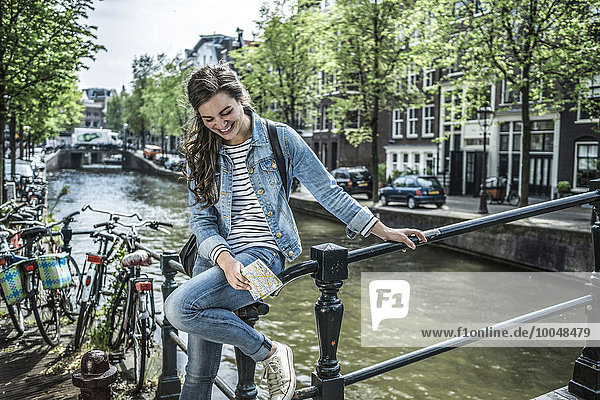 Niederlande  Amsterdam  lachende Touristin mit Stadtplan vor dem Stadtkanal