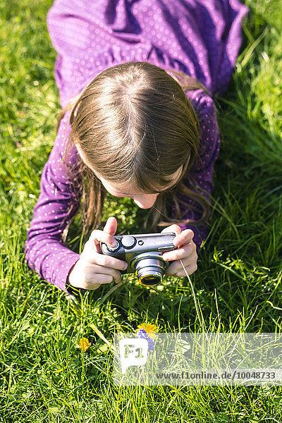 Kleines Mädchen  das auf der Wiese liegt und eine Blume fotografiert.