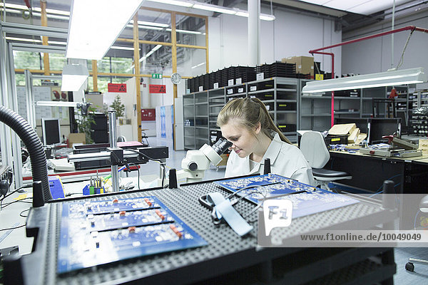 Technician examining circuit board with microscope