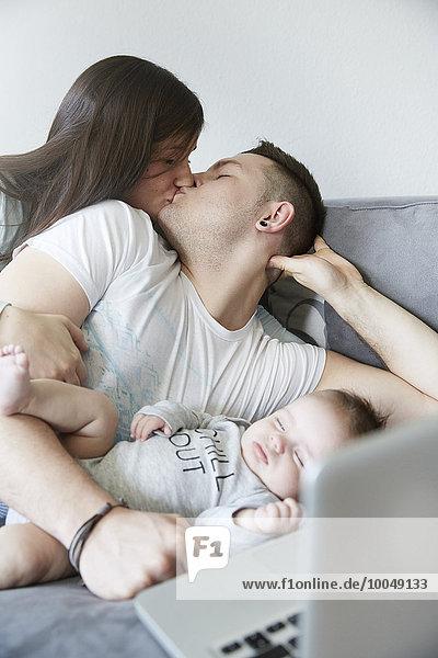 Junger Mann und Frau beim Küssen mit Baby auf der Couch liegend