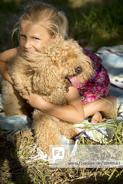 Fröhliches Mädchen umarmt Hund auf Decke