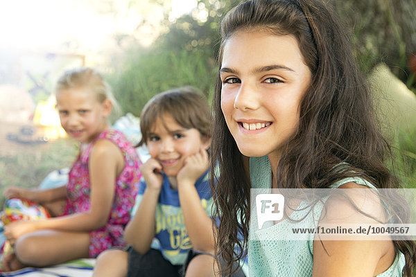 Porträt eines lächelnden Mädchens im Freien mit Geschwistern im Hintergrund