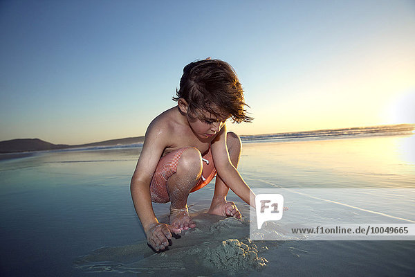 Junge spielt am Strand bei Sonnenuntergang
