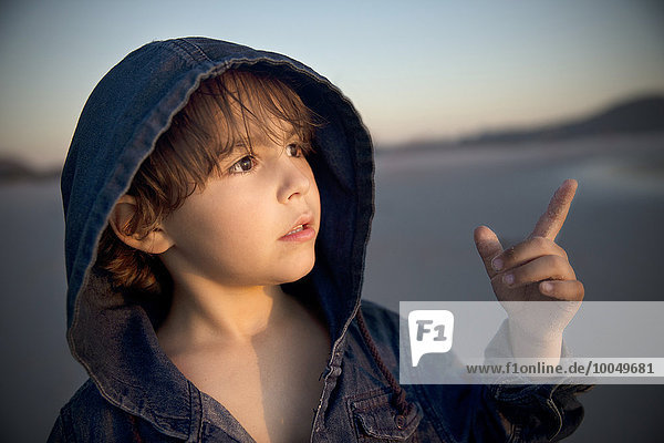 Junge am Strand der mit dem Finger zeigt