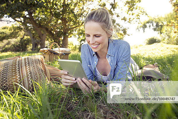 Lächelnde Frau mit digitalem Tablett auf der Wiese liegend