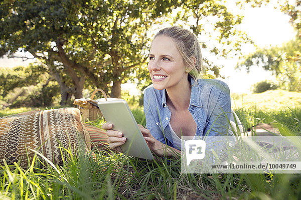 Lächelnde Frau mit digitalem Tablett auf der Wiese liegend