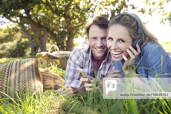 Glückliches Paar auf der Wiese mit einer Frau  die Musik vom Smartphone hört.