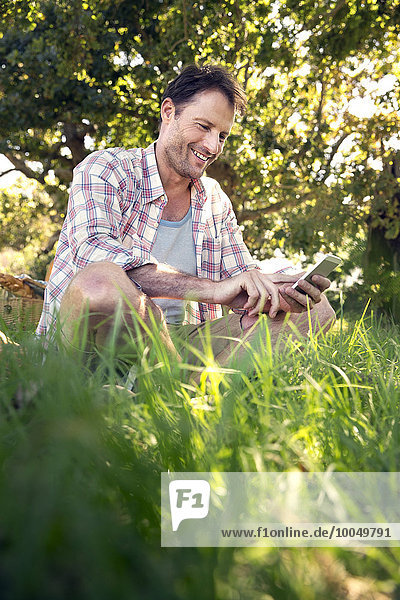 Lächelnder Mann mit Handy auf der Wiese sitzend