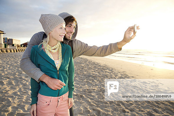 Junges Paar bei Sonnenaufgang mit einem Selfie am Strand