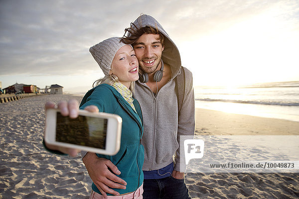 Young couple taking a selfie on beach at sunrise