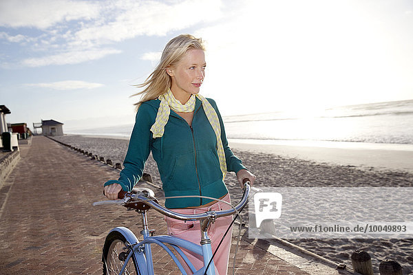 Lächelnde junge Frau mit Fahrrad an der Strandpromenade