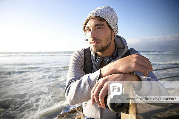 Junger Mann mit Longboard an der Küste