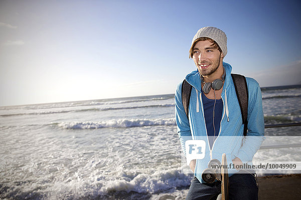 Lächelnder junger Mann mit Longboard an der Küste