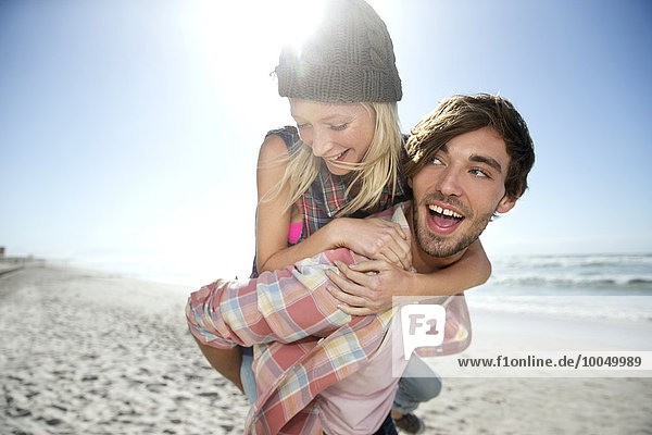 Junger Mann mit Freundin Huckepack am Strand