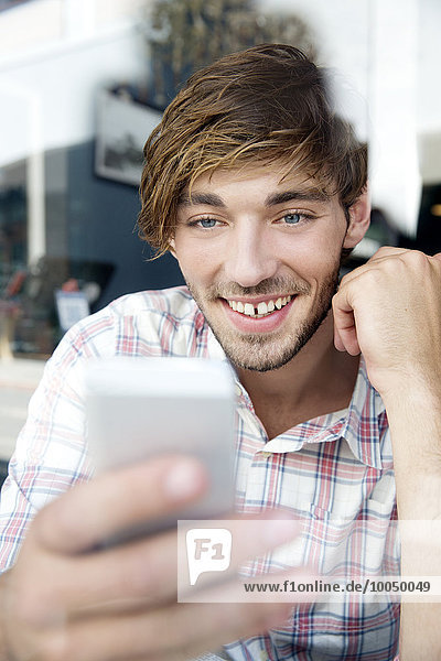 Smiling young man in a cafe looking on cell phone
