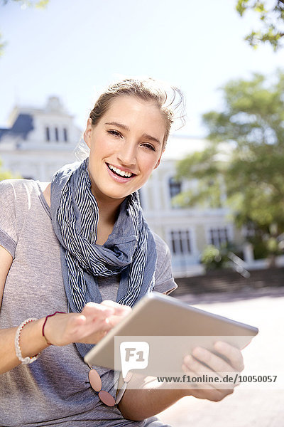 Porträt einer lächelnden jungen Frau mit digitalem Tablett im Freien
