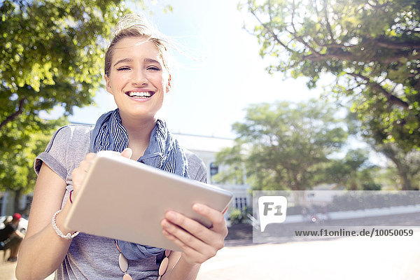 Lächelnde junge Frau mit digitalem Tablett im Freien