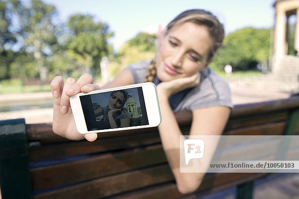 Junge Frau auf Parkbank mit einem Selfie