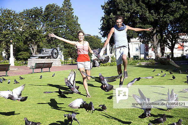 Begeistertes junges Paar jagt Tauben im Park