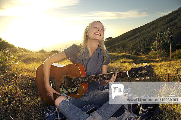 Happy young woman playing guitar on blanket in meadow