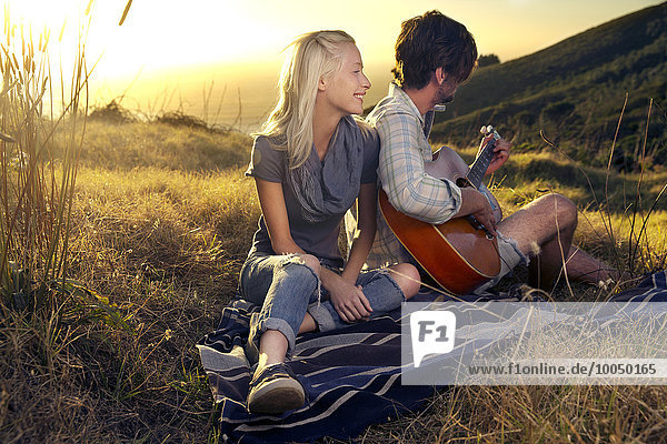 Young couple with guitar on blanket in meadow