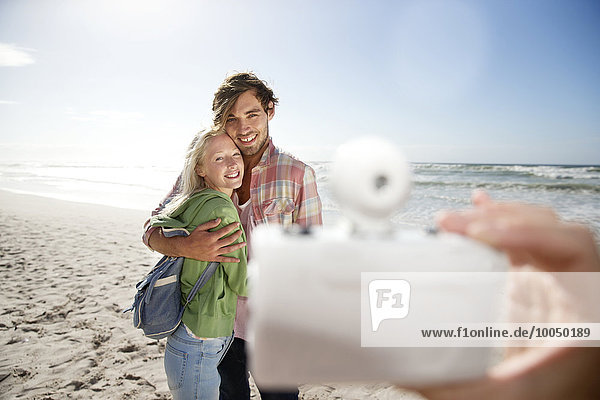 Glückliches junges Paar am Strand beim Fotografieren