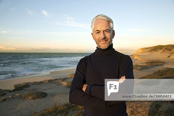 South Africa  portrait of white haired man wearing turtleneck standing on beach dunes before sunrise