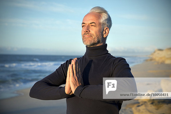 Südafrika  Porträt eines Mannes mit Rollkragenpulli  der vor Sonnenaufgang am Strand meditiert.