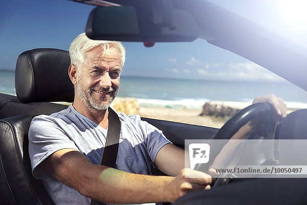 South Africa  portrait of smiling man sitting in a convertible in front of the beach