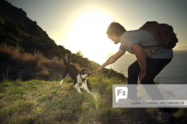 Südafrika  Mann spielt mit Hund an der Küste bei Sonnenuntergang