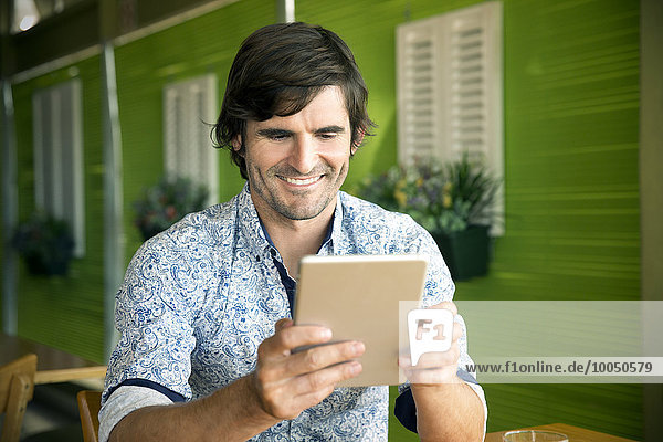 Porträt eines lächelnden Mannes mit digitalem Tablett im Cafe