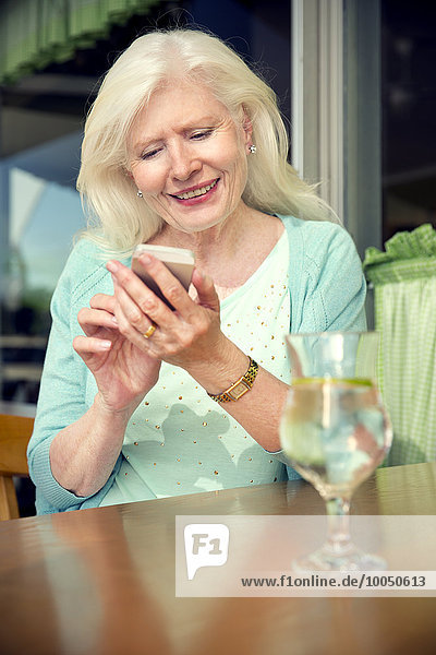 Porträt einer glücklichen Seniorin die mit dem Smartphone in einem Café sitzt.