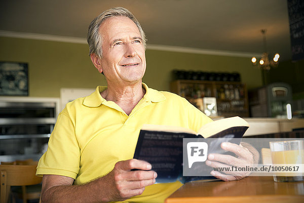 Porträt eines glücklichen älteren Mannes  der in einem Café mit einem Buch sitzt.