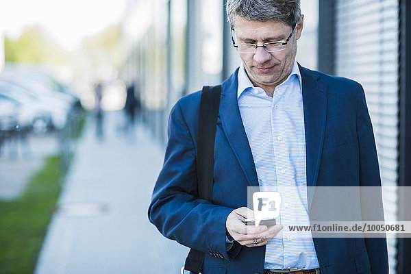 Deutschland Portrait eines reifen Geschäftsmannes in der Straße mit Smartphone