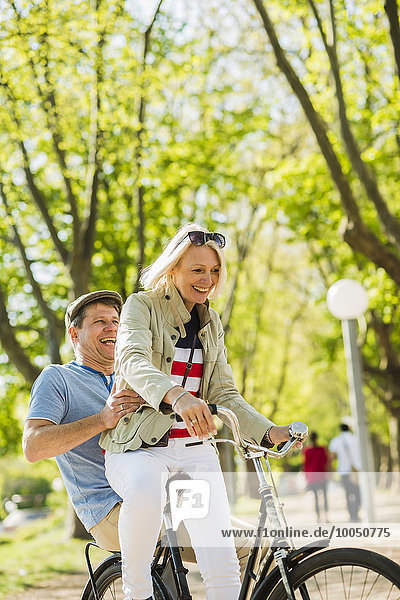 Mature couple riding bike in park  man sitting on rack