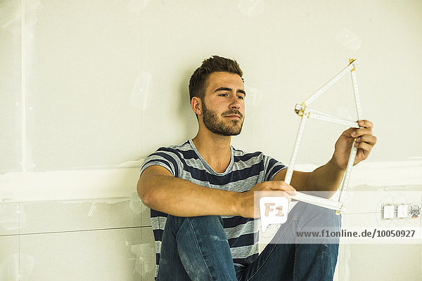 Young man sitting at blank wall holding pocket rule