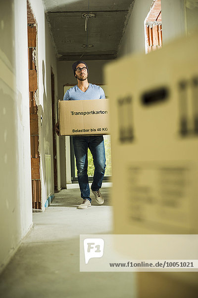 Young man carrying cardboard box in hallway
