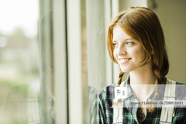 Lächelnde junge Frau schaut aus dem Fenster.