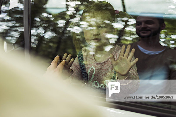 Mädchen im Auto mit Blick auf Vater hinter der Fensterscheibe