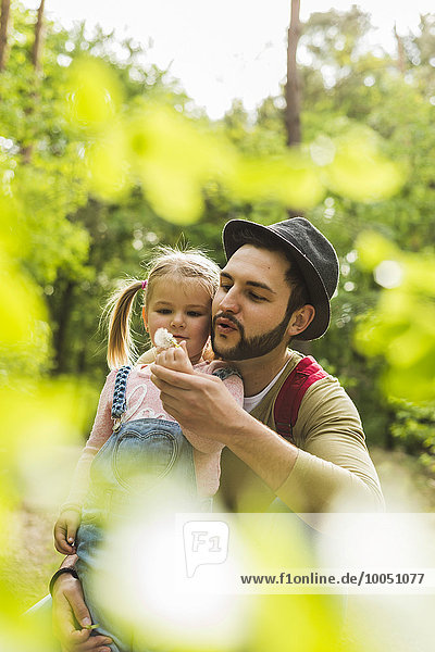 Vater und Tochter mit Pusteblume im Wald
