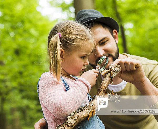 Girl with father in forest examining branch with magnifier