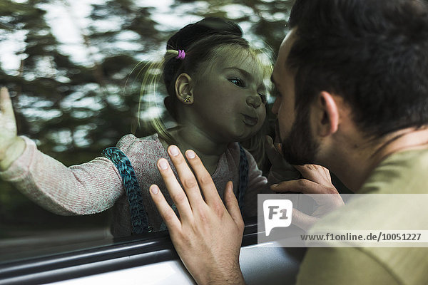 Mädchen im Auto küsst Vater hinter der Fensterscheibe