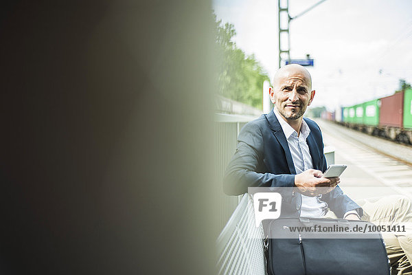 Businessman holding cell phone on railway platform