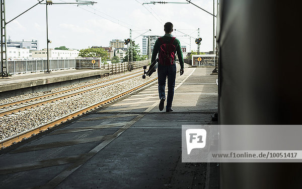 Junger Mann mit Skateboard läuft auf Bahnsteig