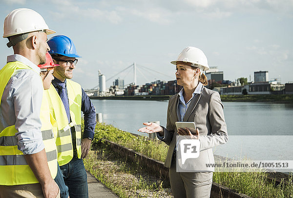 Businesswoman talking to people with safety helmets at riverside