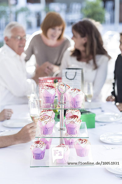 Pink cup cakes on cake stand on restaurant table  people talking in background