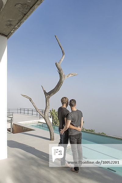Schwules Paar auf einer Terrasse am Pool stehend